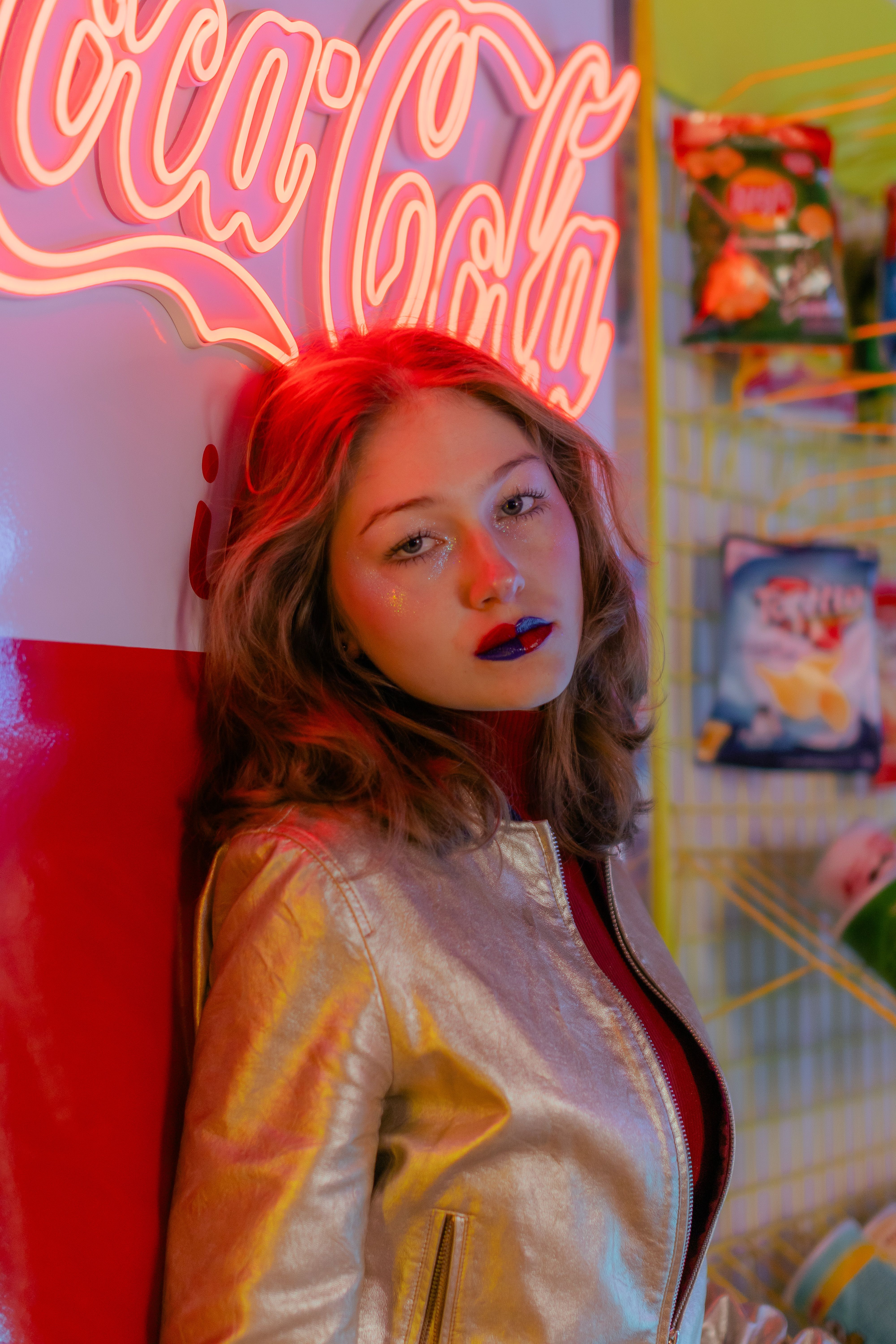 Portrait of a woman leaning against a Coca-Cola sign under neon lights indoors.