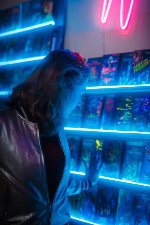 Free A woman browsing vinyl records in a neon-lit retro store, wearing a metallic jacket. Stock Photo