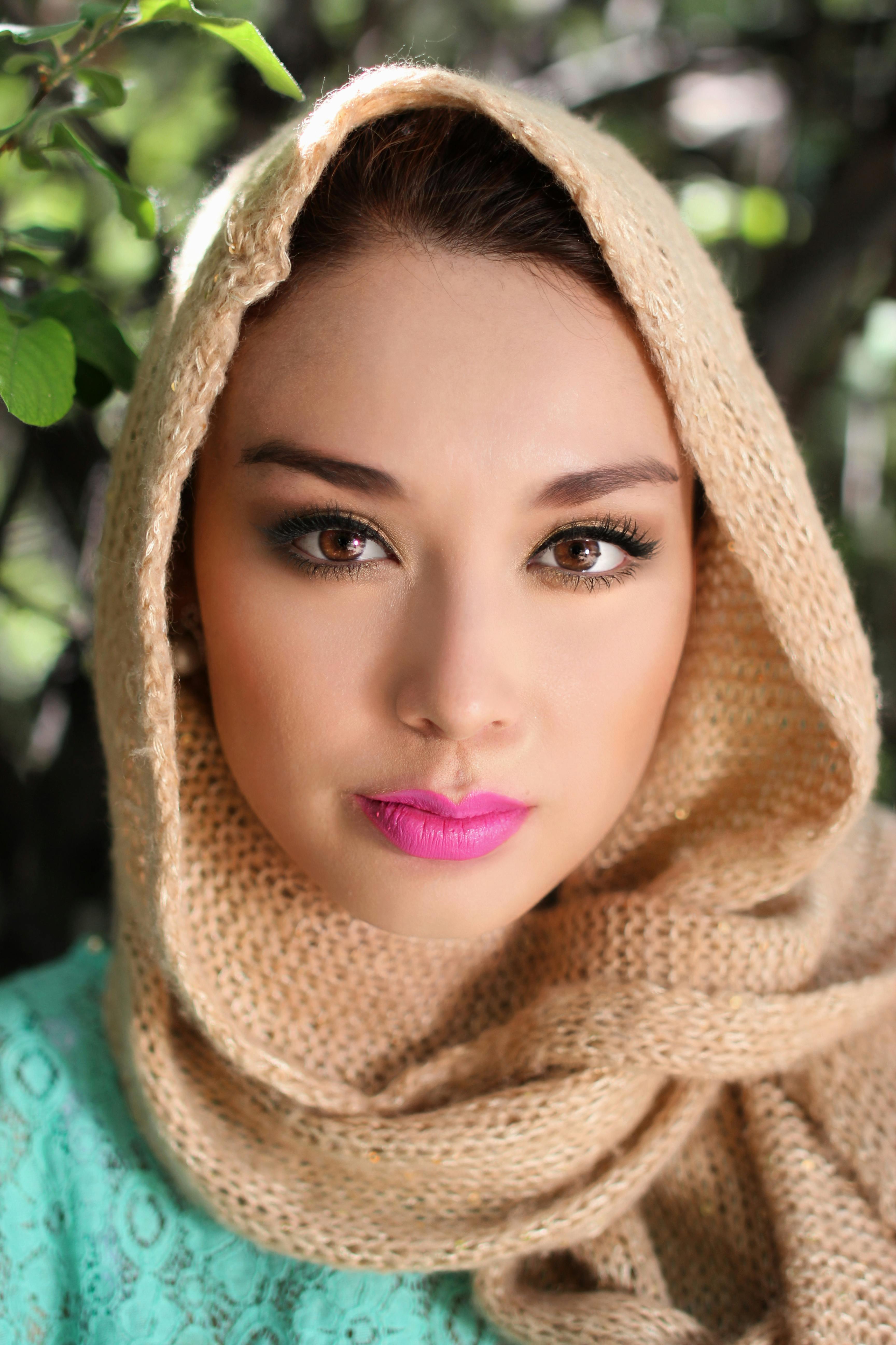 Striking outdoor portrait of a woman in a hijab showcasing vibrant makeup and natural surroundings.