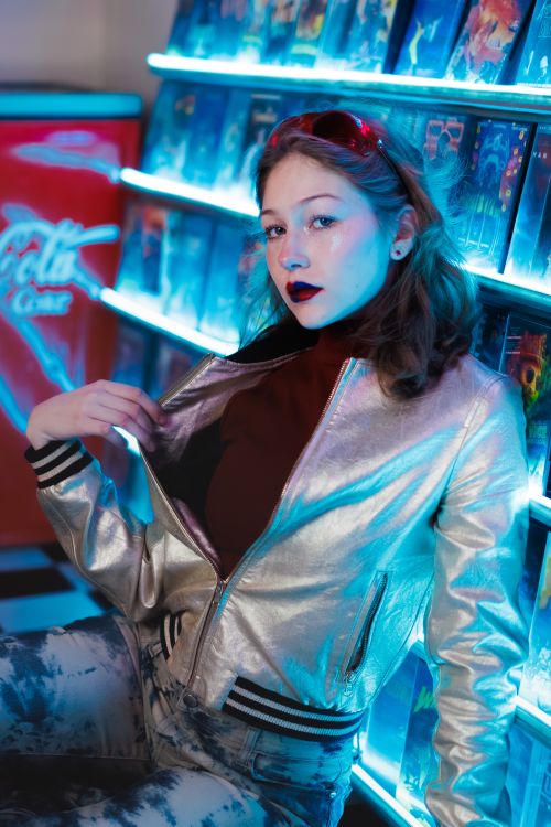 Free Stylish woman posing in metallic jacket at a vibrant retro arcade with neon lights. Stock Photo