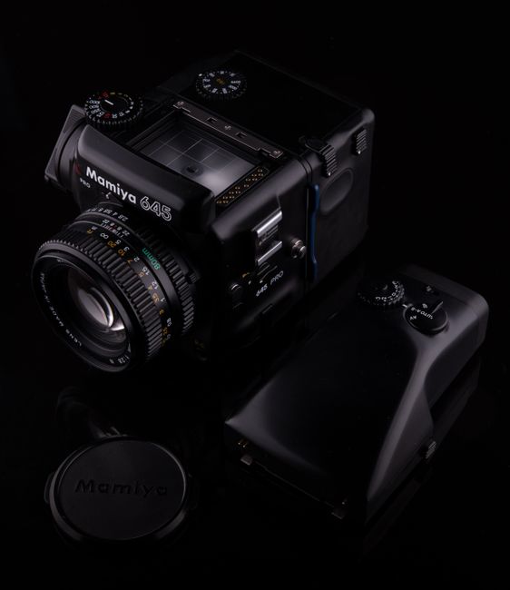 Close-up of a Mamiya 645 Pro medium format camera with a lens on a black studio background.