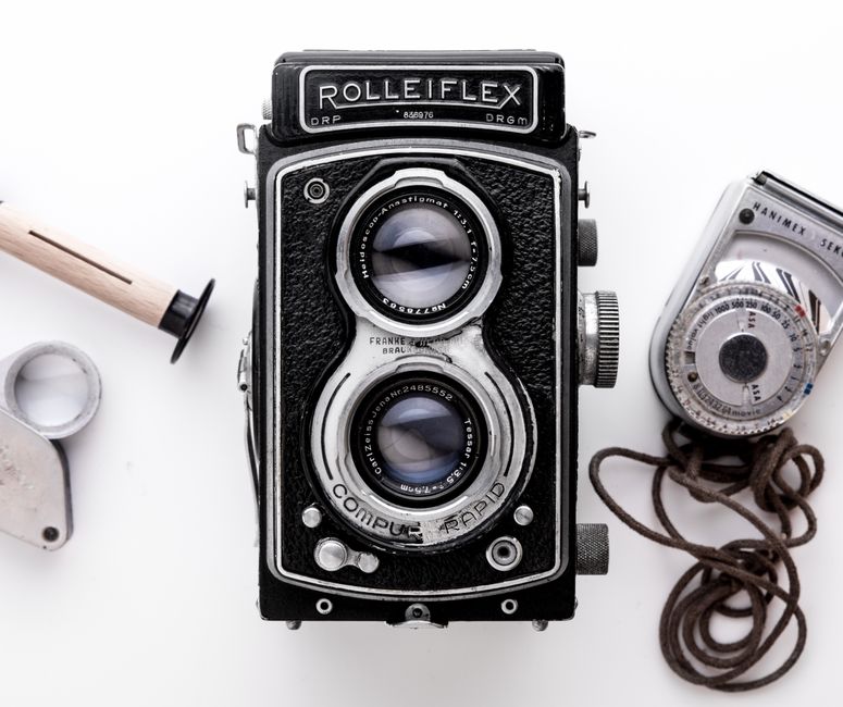 Close-up of a vintage Rolleiflex camera with retro photography equipment on a white background.