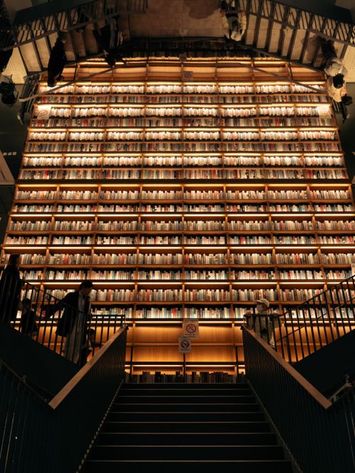 Free A grand interior view of a bookstore with floor-to-ceiling illuminated shelves stacked with books. Stock Photo