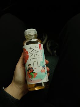 Close-up of a hand holding an Asian drink bottle against a dark background.