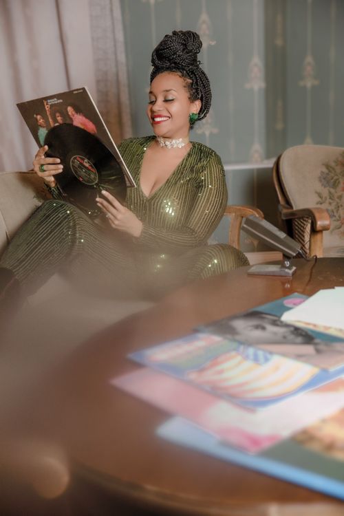 Free Black woman in green clothes smiling while holding a vinyl record. Indoor fashion scene. Stock Photo