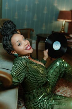 Stylish woman in green sequined outfit holding a vinyl record indoors, smiling.