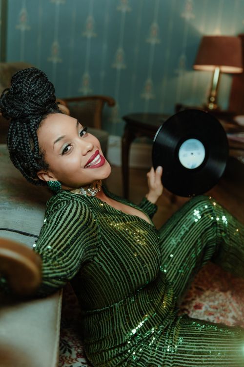 Free Stylish woman in green sequined outfit holding a vinyl record indoors, smiling. Stock Photo