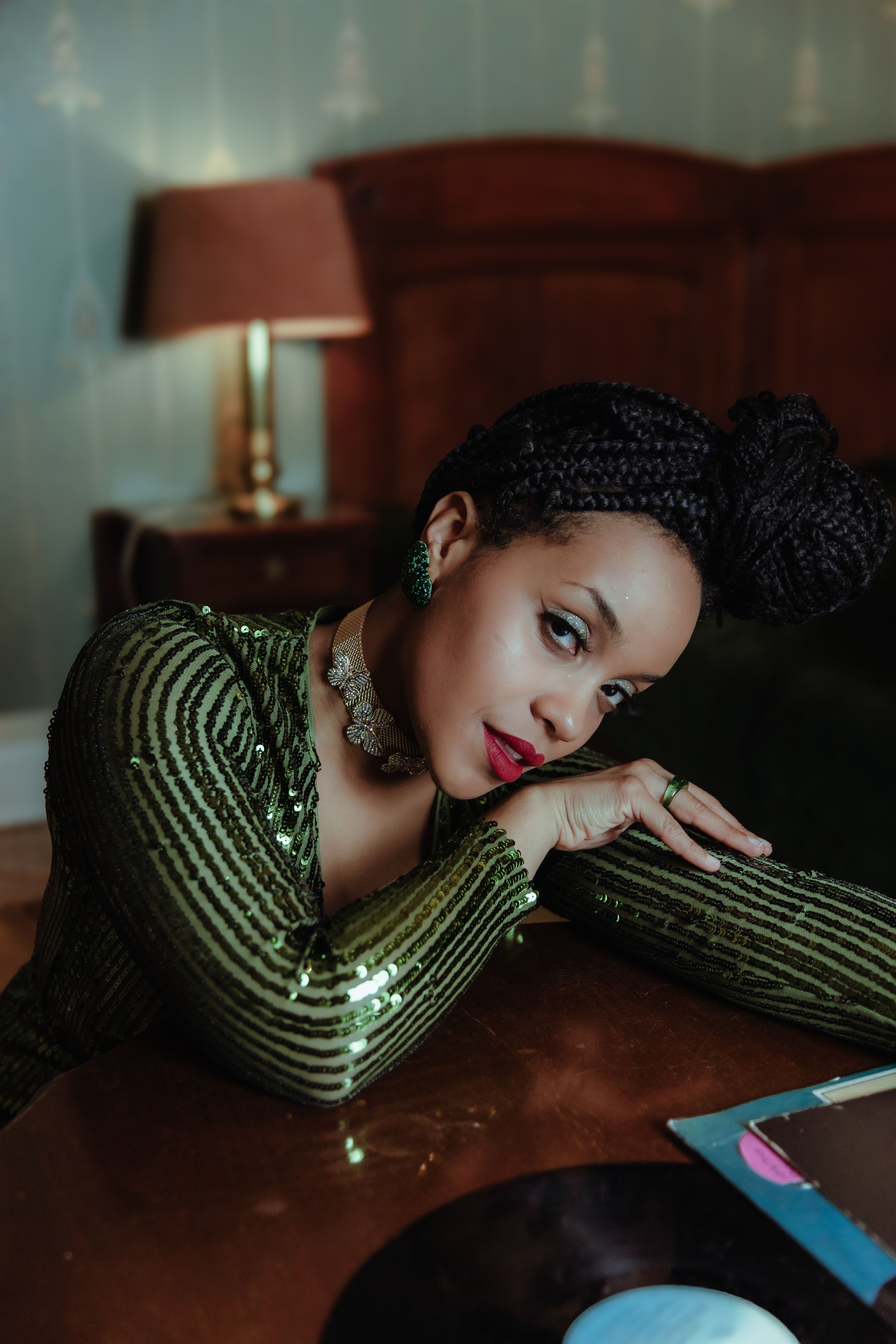Stylish portrait of a woman in a green sequin dress leaning gracefully on a table indoors.