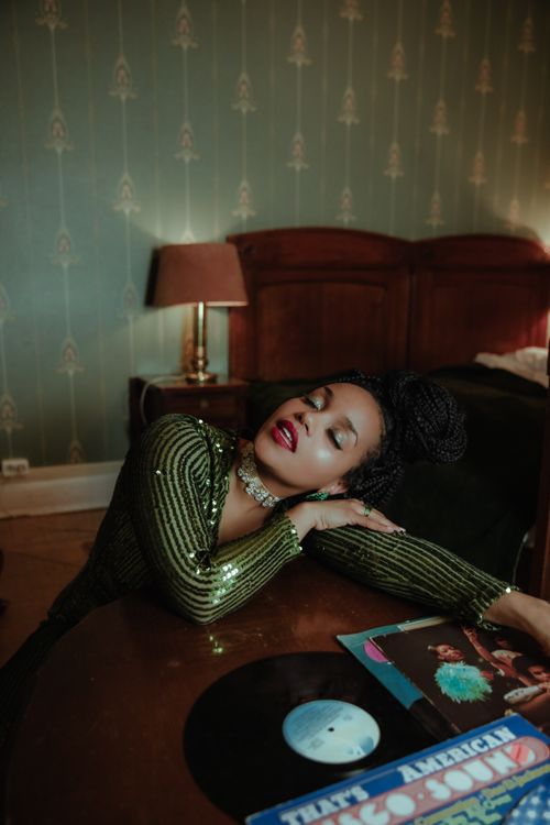 Free A stylish woman in a glamorous setting, posed with vintage vinyls on a wooden table. Stock Photo