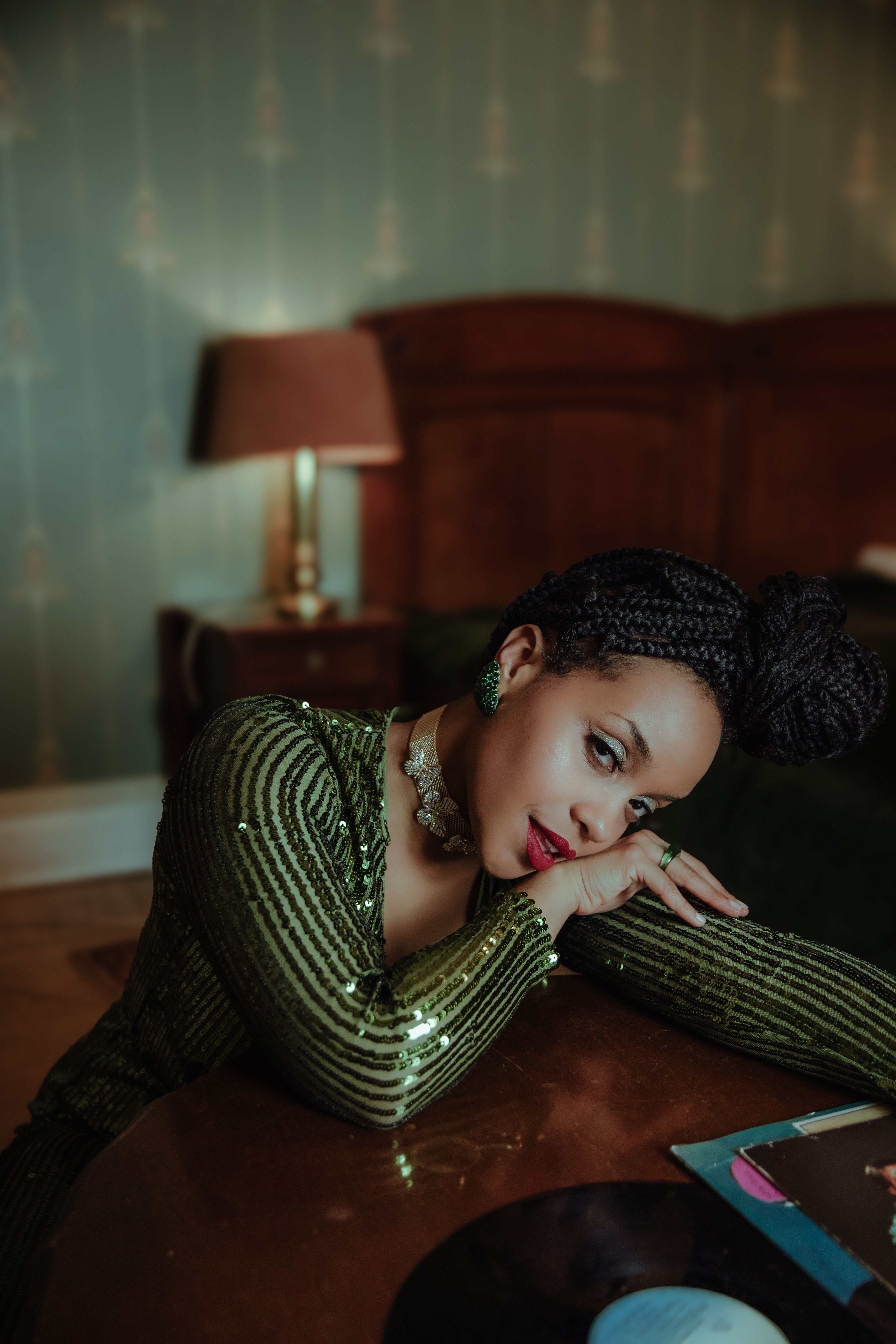 Captivating fashion portrait of a stylish black woman in a luxurious indoor setting, wearing a green sequined outfit.