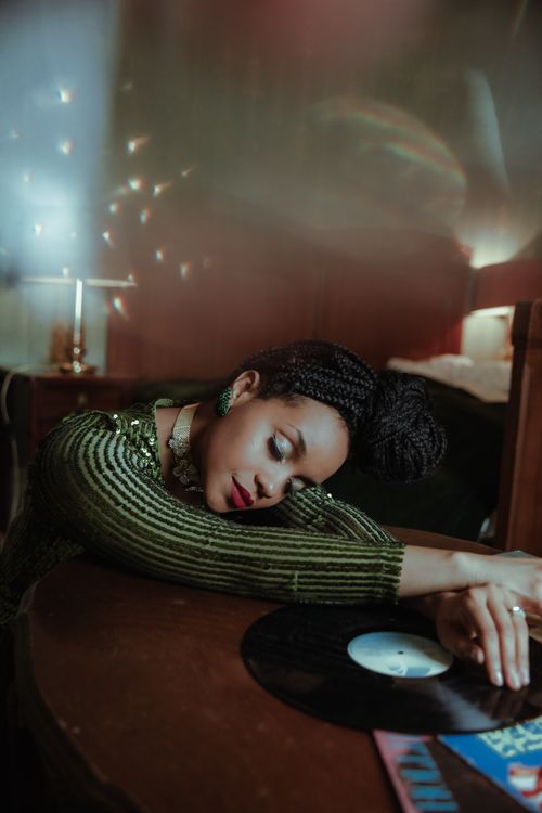 Free A woman in a green sweater peacefully leaning on a table with a vinyl record nearby. Stock Photo