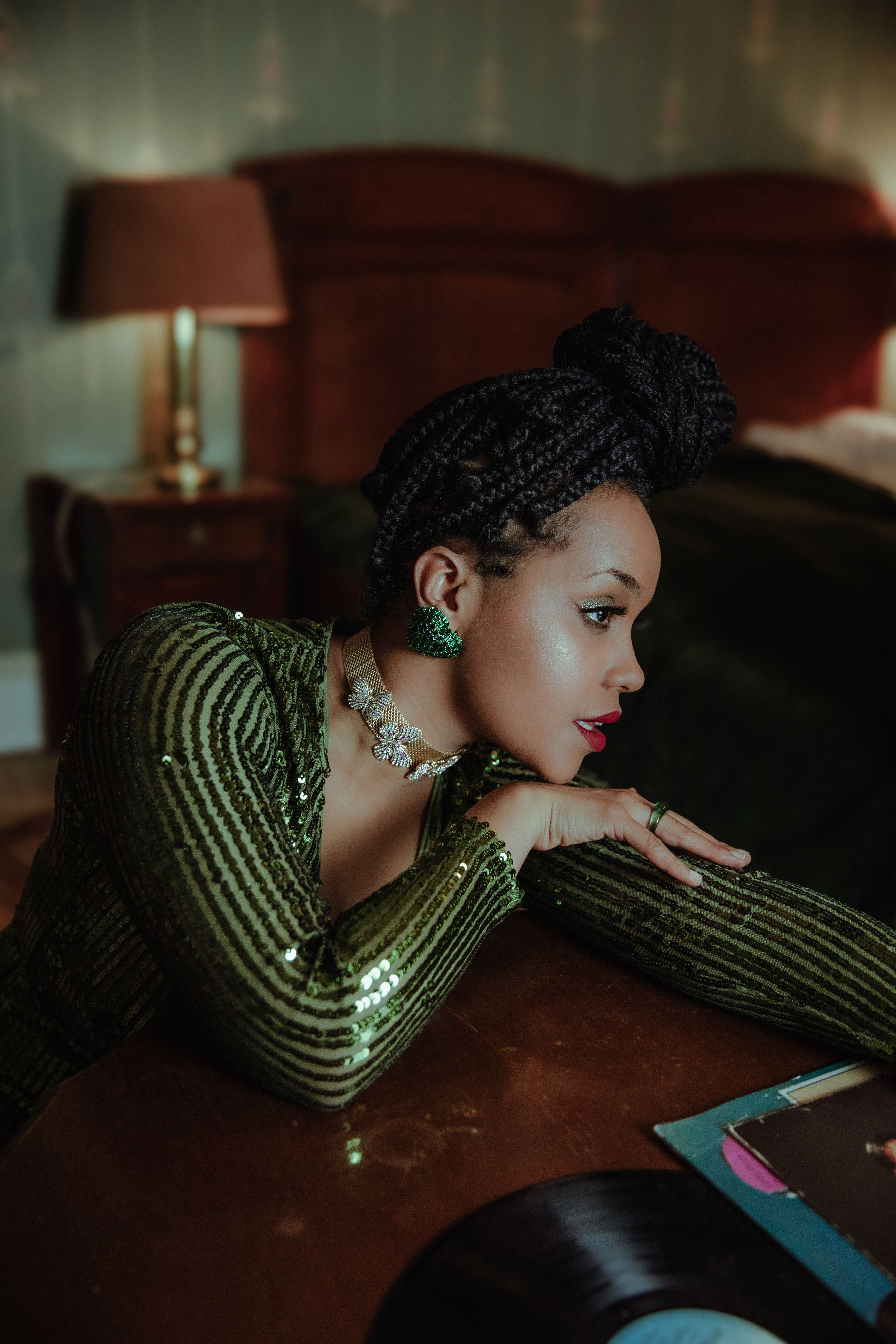 Stylish woman in green outfit leaning on a table, embracing fashion and elegance indoors.
