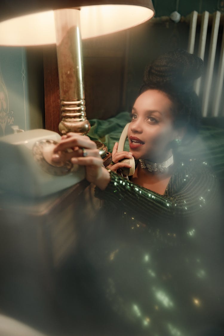 Woman In A Green Dress Talking On The Phone Sitting By The Bed