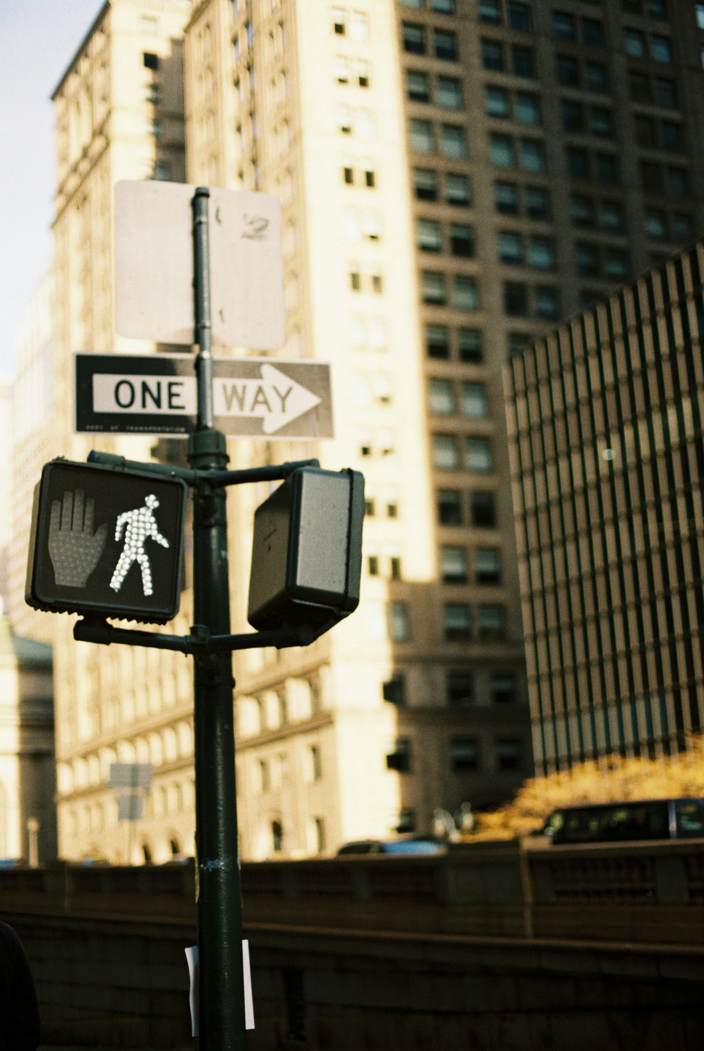 City street corner with a one way sign and pedestrian signals in urban downtown.