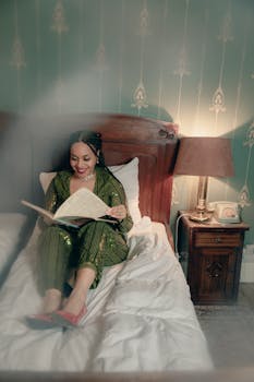 A woman in a green jumpsuit relaxes on a bed and reads, exuding vintage charm.