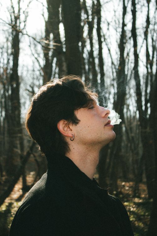 Free A side profile of a man relaxing while smoking in a serene autumn forest setting. Stock Photo
