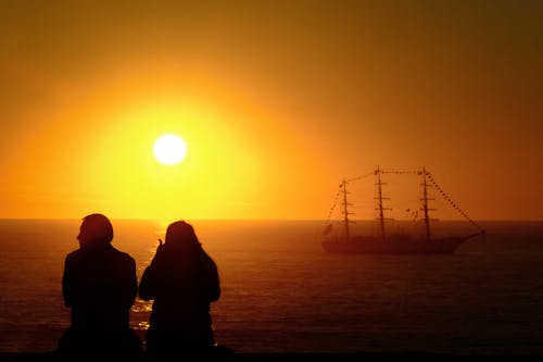 Silhouettes of a Man and Woman Sitting on a Shore at Sunset