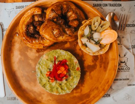 Top view of Mexican cuisine featuring guacamole, buns, and assorted vegetables on a wooden plate.
