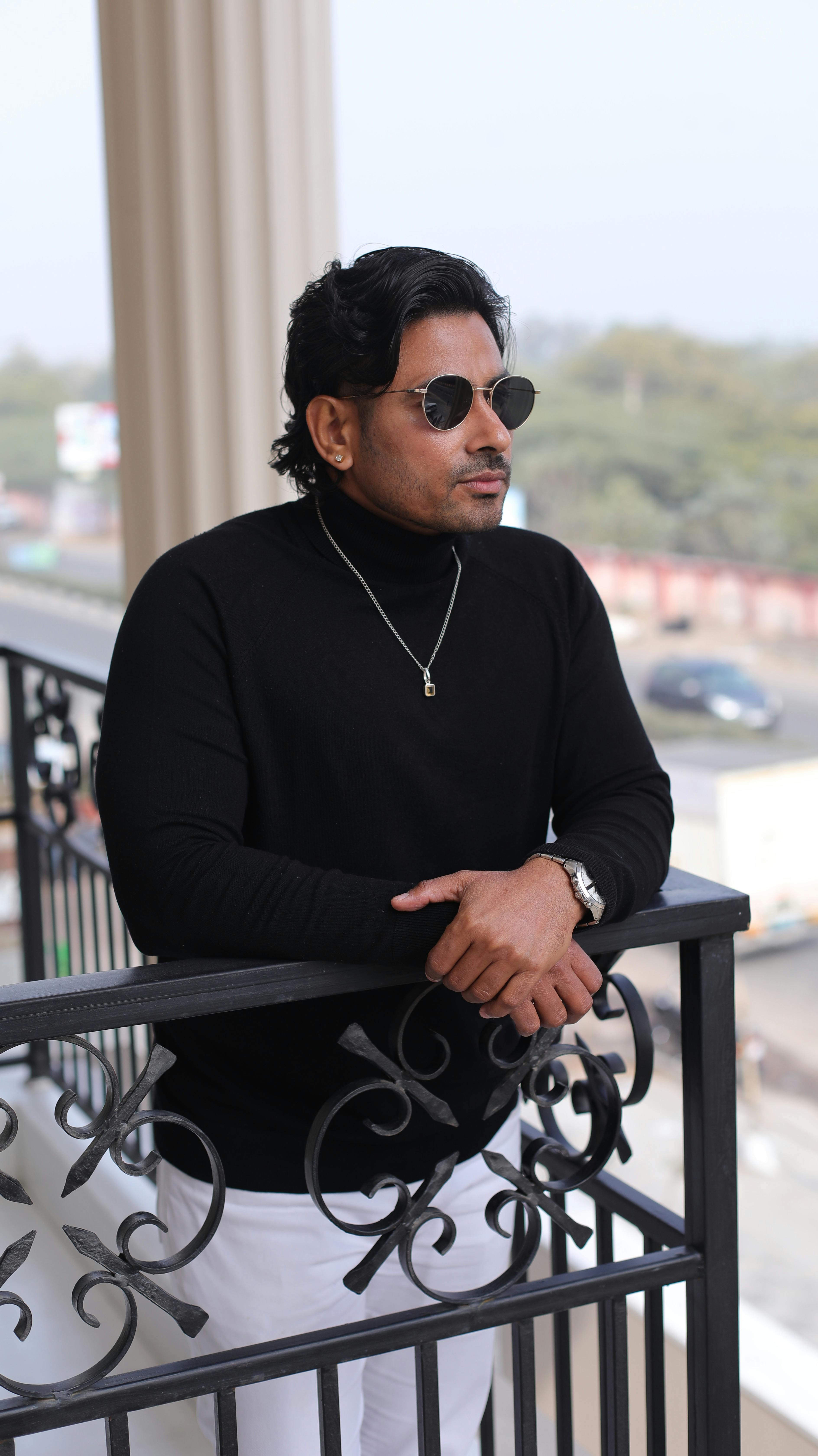 Fashionable man in sunglasses and black top on a railing, Jaipur, India.