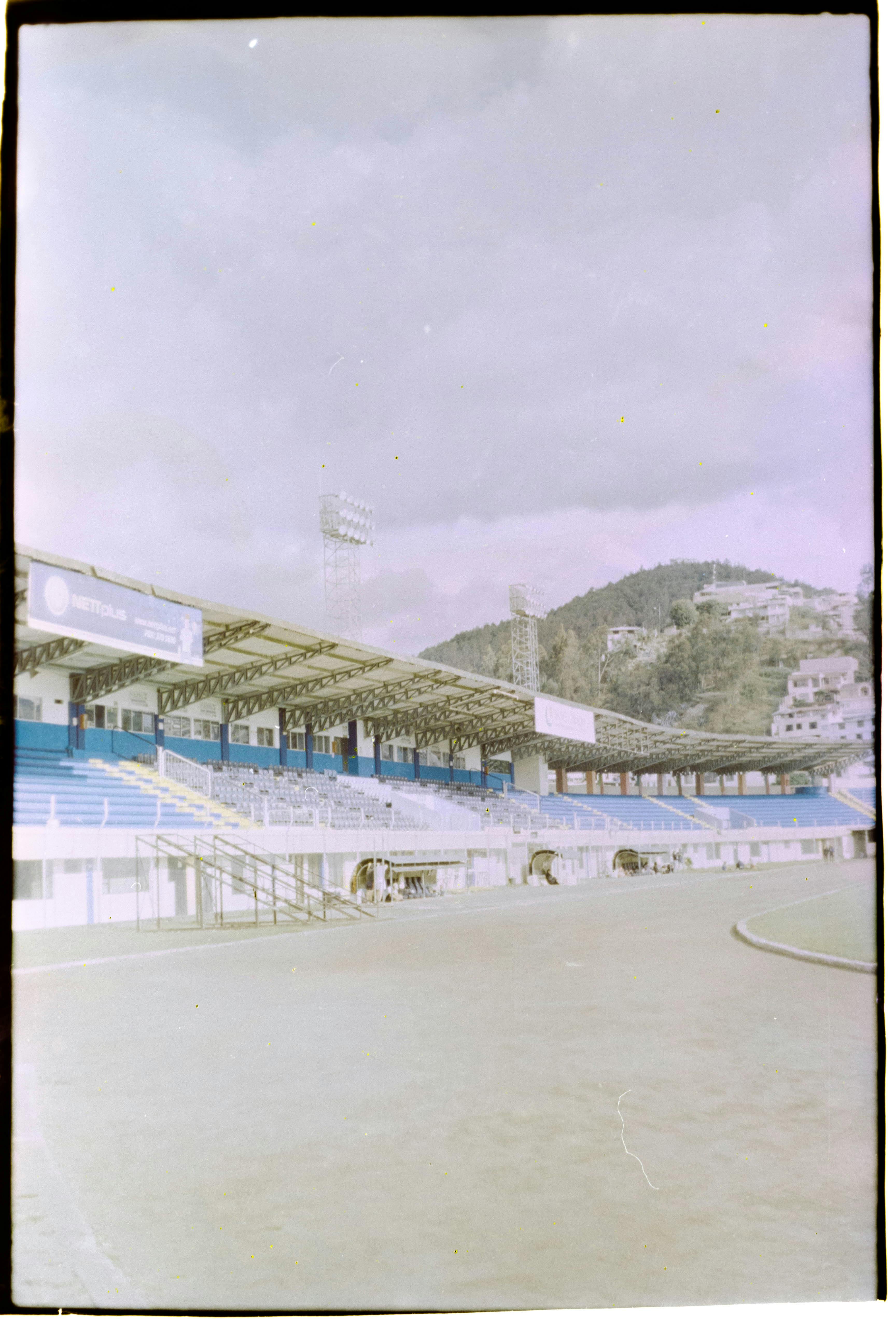 A vacant stadium with blue tiered seating under a cloudy sky, perfect for sports events.