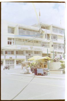 Vibrant street market with stalls outside a municipal building on a sunny day.