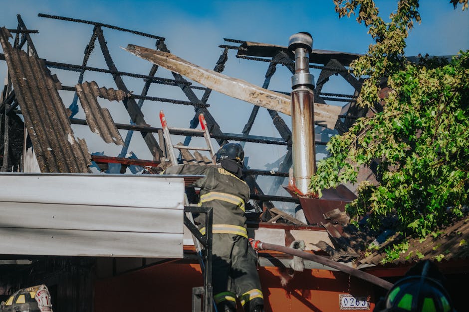 A firefighter tackles the aftermath of a house fire, clearing debris from a burned roof.