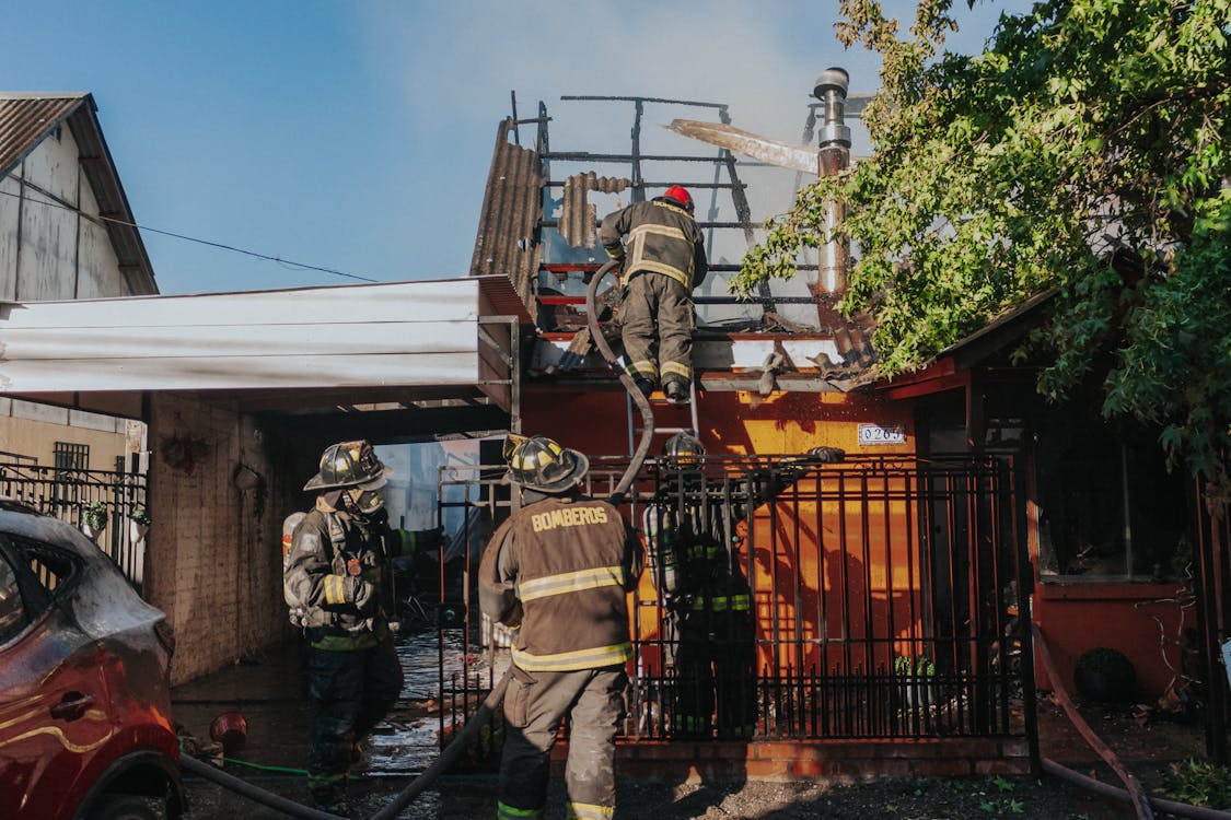Free Firefighters working to extinguish a house fire, showcasing bravery and teamwork outdoors. Stock Photo