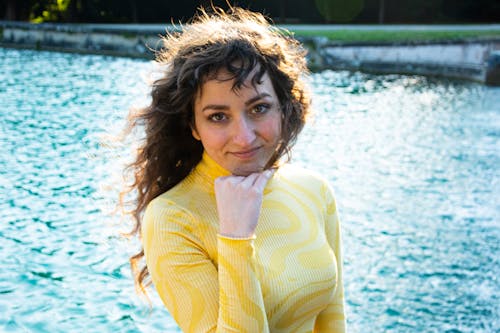 A woman in a yellow top posing near a body of water