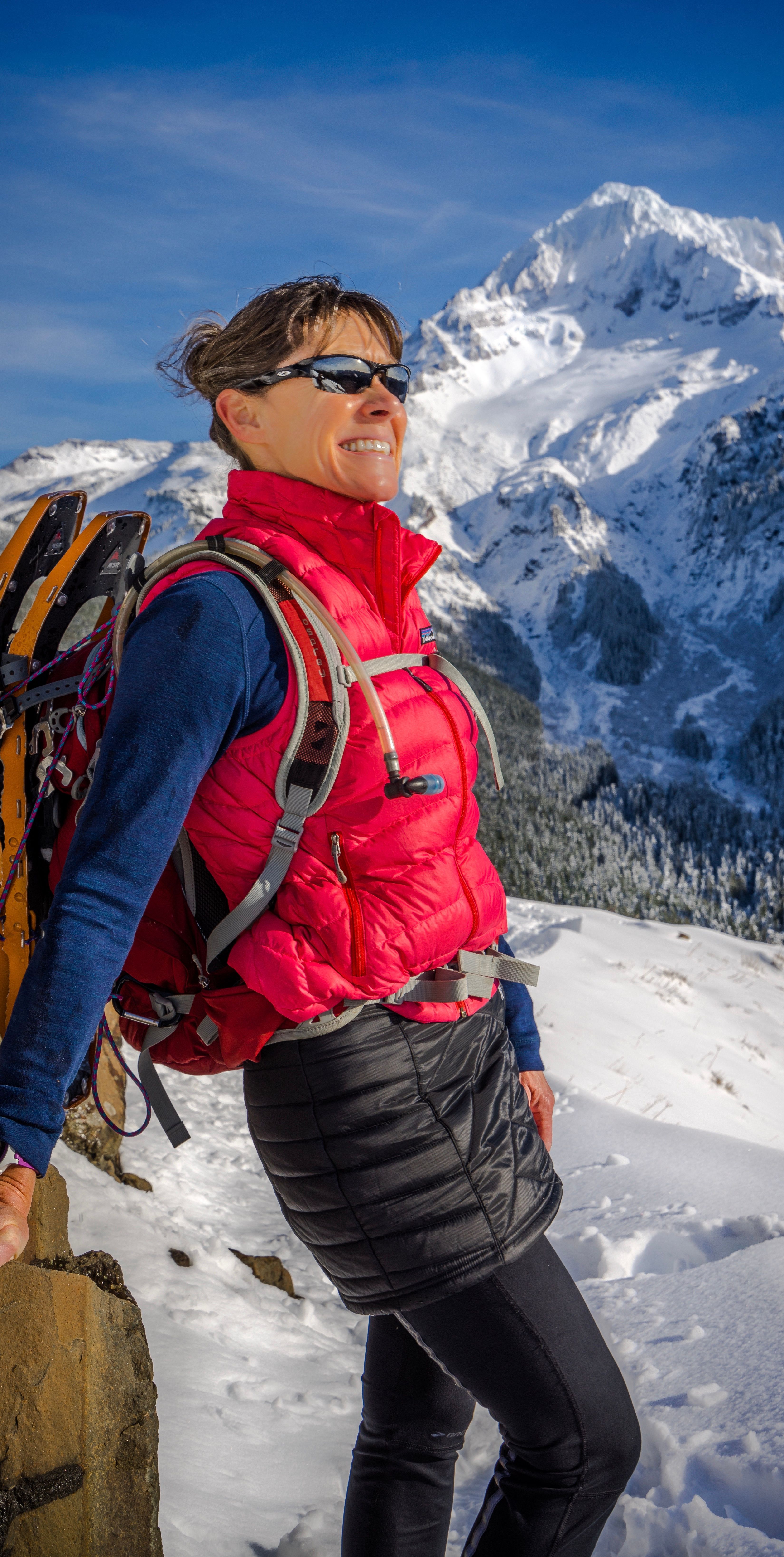 A woman smiles while hiking in snow-covered mountains, enjoying winter adventure.