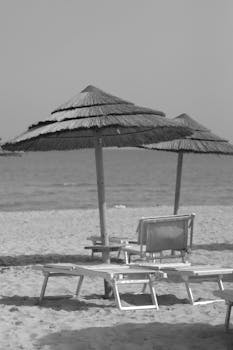 Peaceful black and white beach scene with straw umbrellas in Catania, Italy.