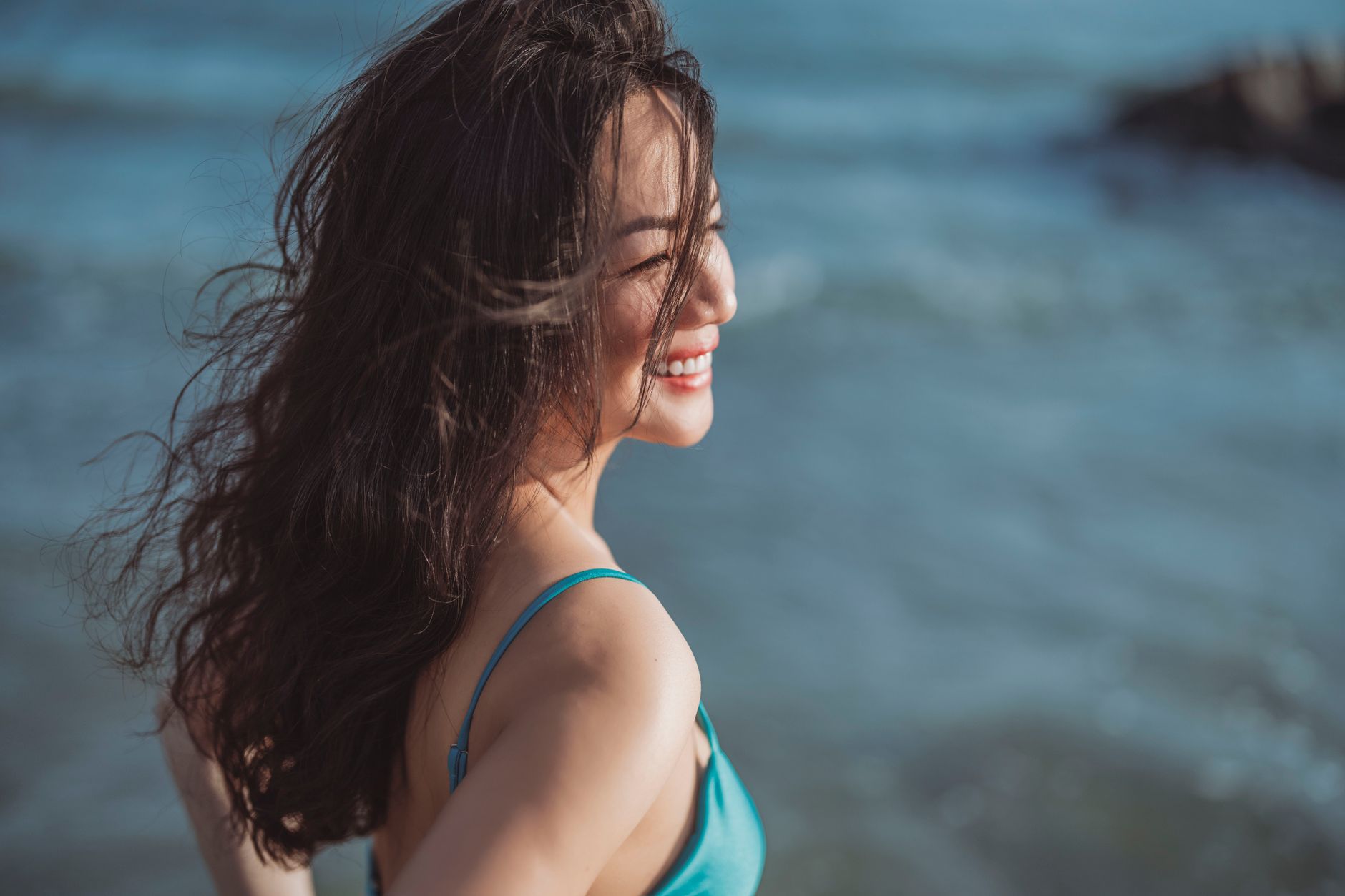 Smiling woman with long hair at the beach, savoring the sun and sea breeze.