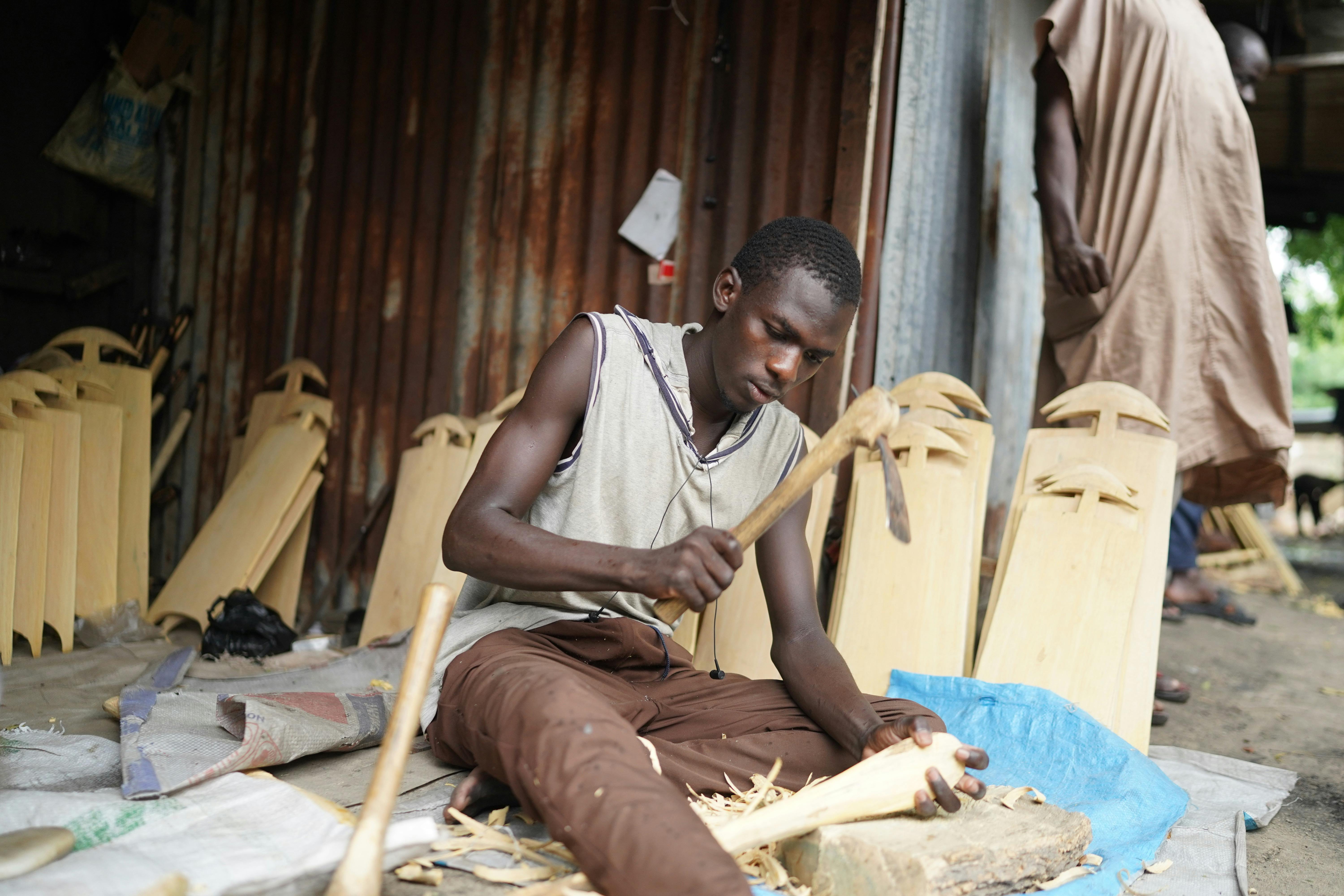 a man sitting on a bench making wooden objects