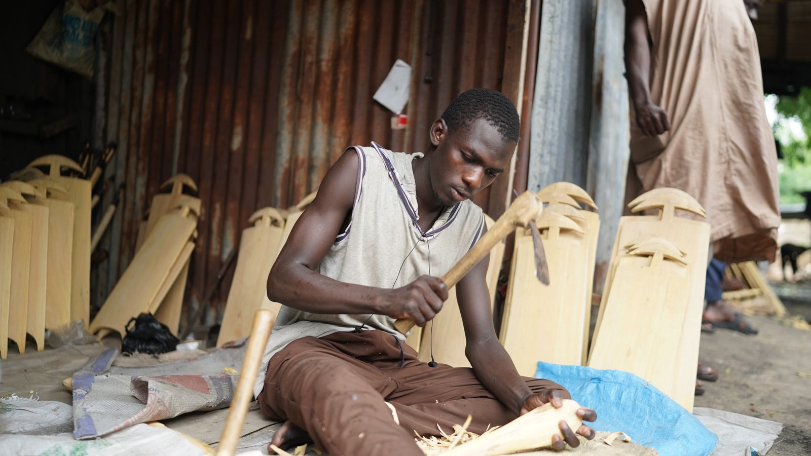 A man sitting on a bench making wooden objects, Gabon
