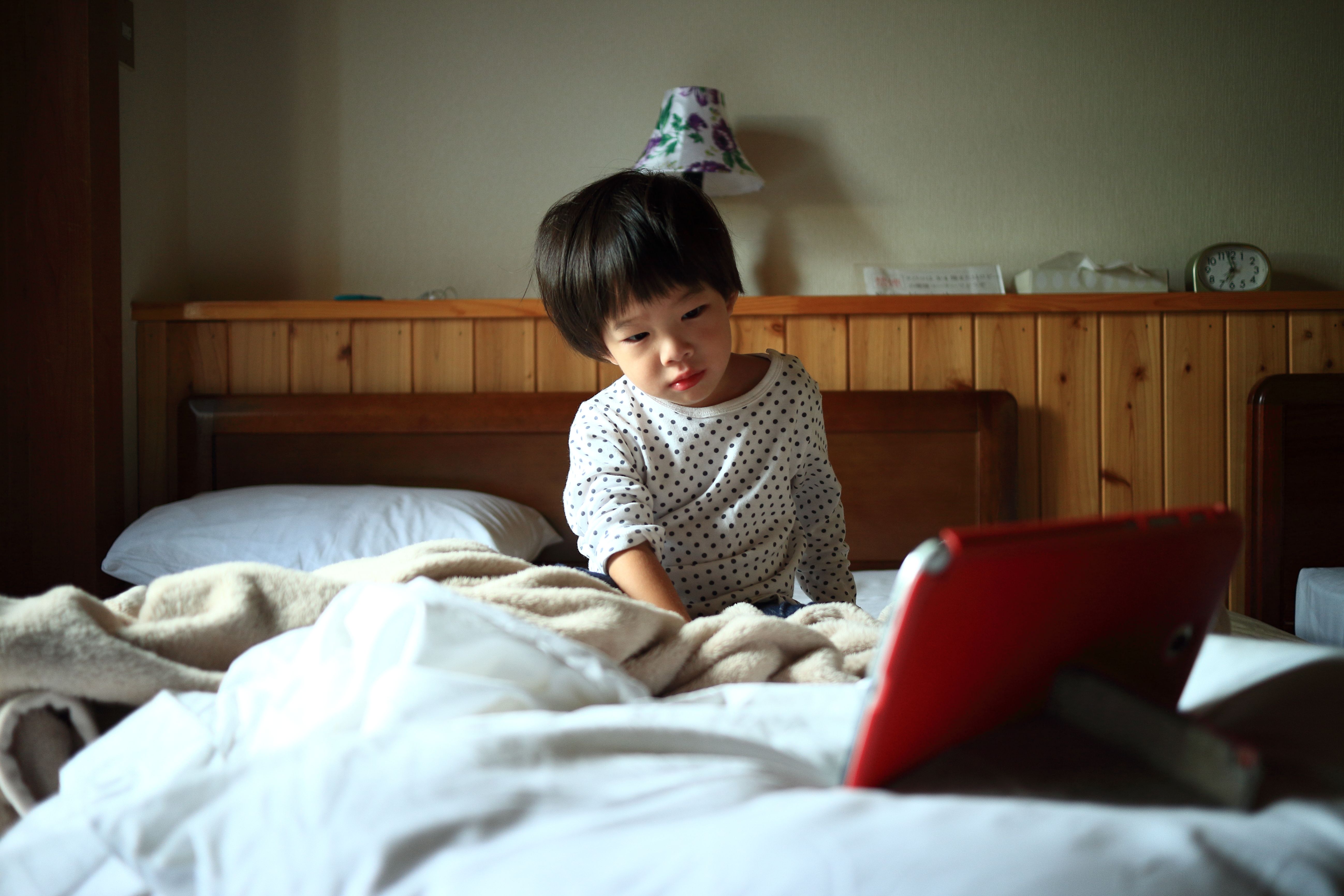 A young child comfortably watching a tablet on a cozy bed in a Nikko hotel room.