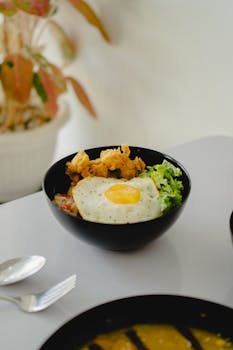 A tempting Indonesian rice bowl featuring a sunny-side-up egg, fresh lettuce, and crispy chicken florals.