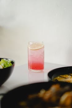 A vibrant pink lemonade with ice, paired with fresh salad and ramen on a table.