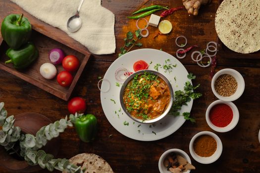A vibrant Indian meal surrounded by spices and fresh vegetables, shot from above.