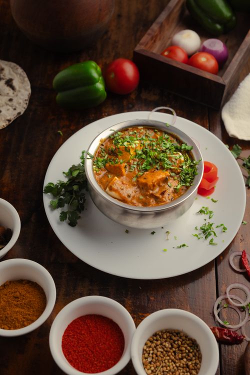 Free Close-up of a flavorful Indian curry with fresh vegetables and spices on a wooden table. Stock Photo