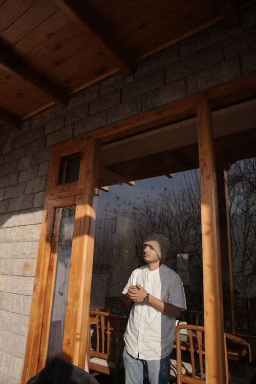 Free A man in casual winter clothing stands by a wooden house, reflecting serene outdoor vibes. Stock Photo