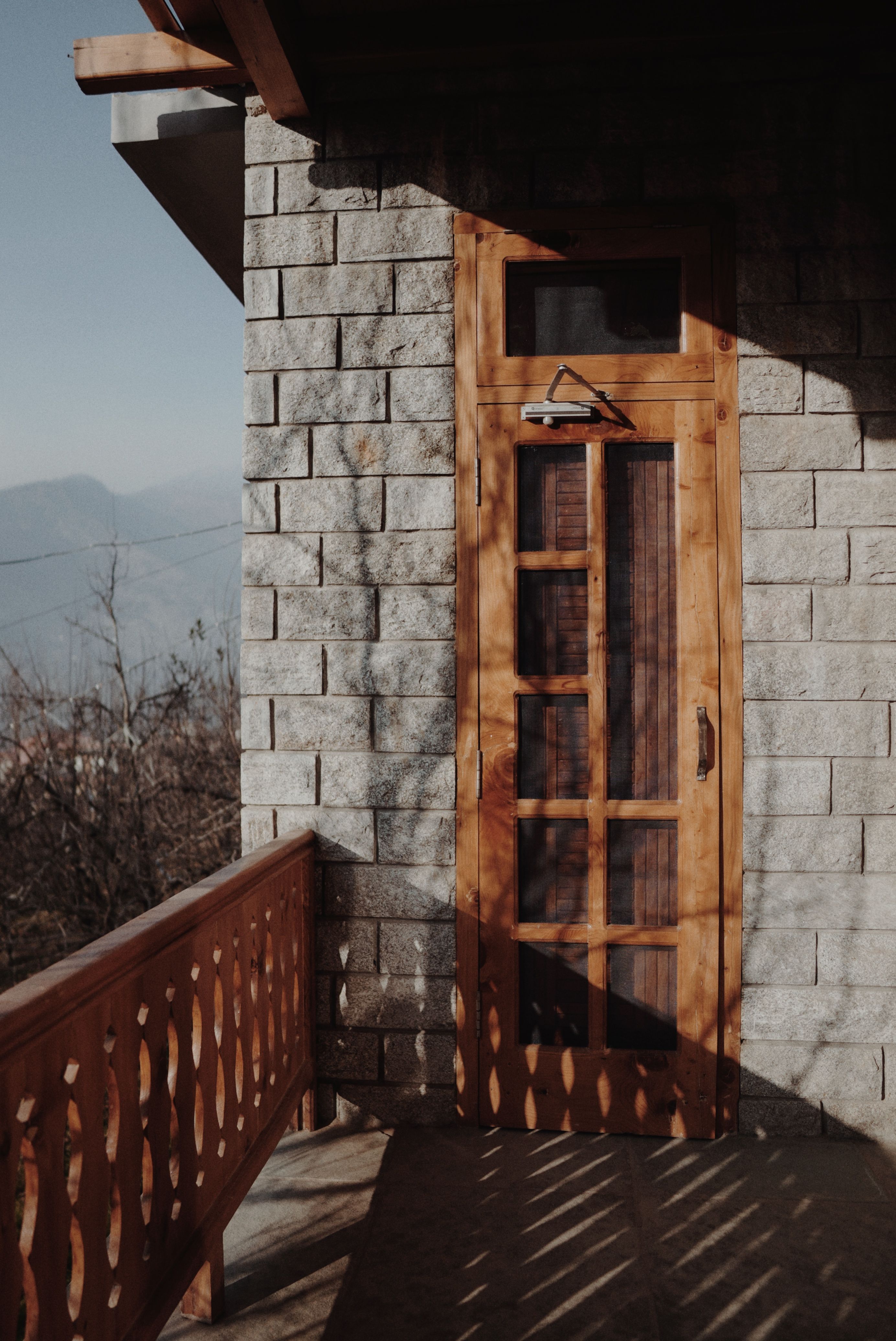 Sunlit stone-walled terrace with a rustic wooden door and decorative railing.