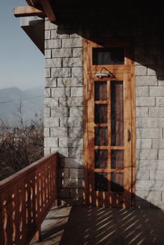 Sunlit stone-walled terrace with a rustic wooden door and decorative railing.