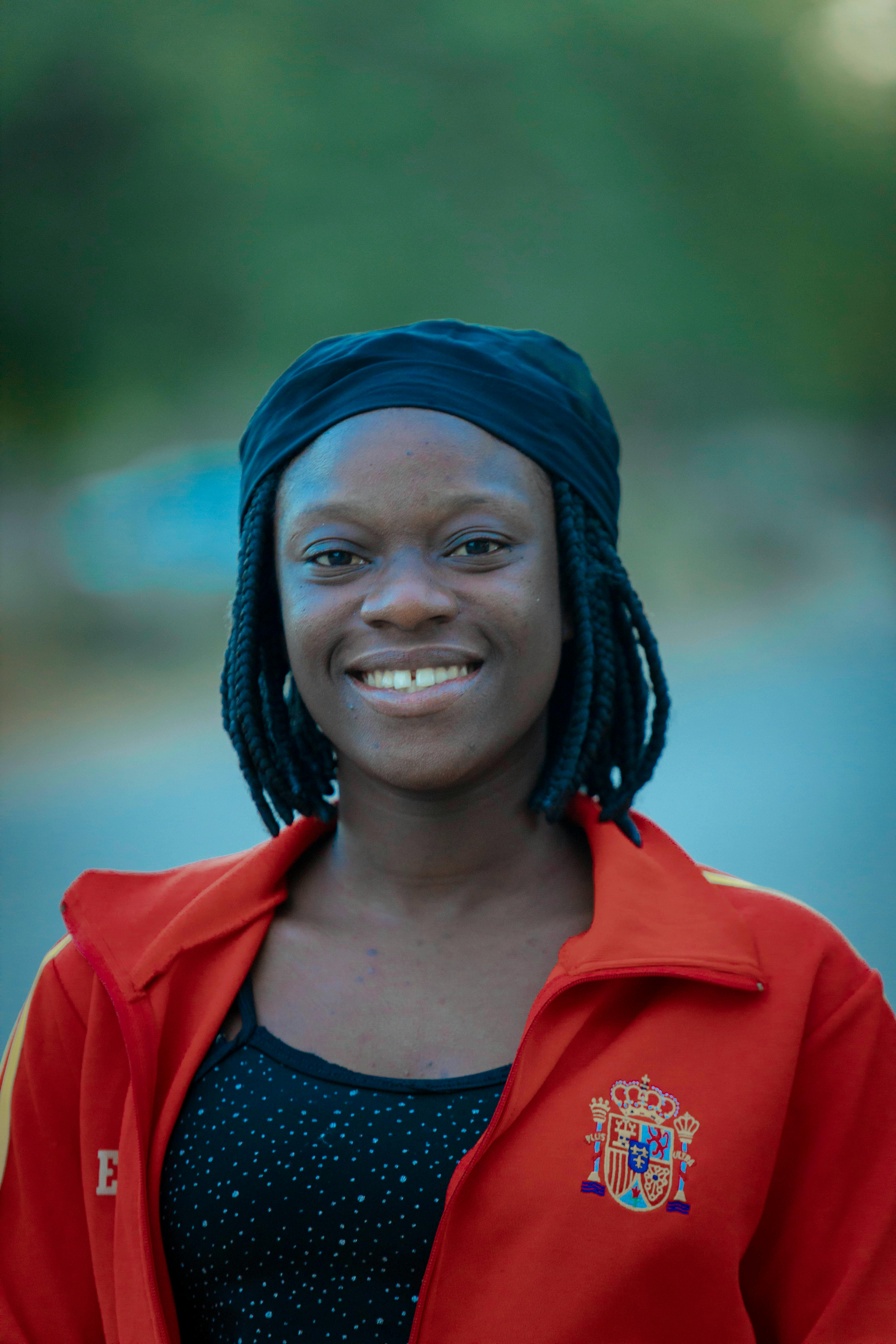 Cheerful woman with dreadlocks smiling in red jacket outdoors.