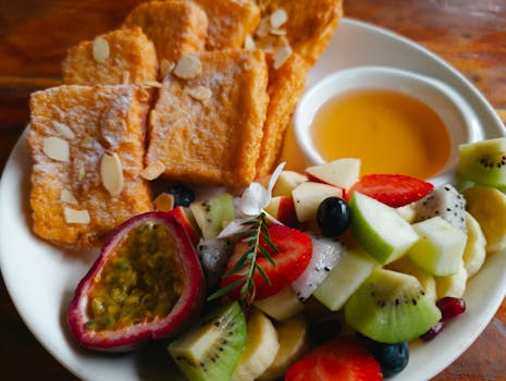 Tasty breakfast plate featuring French toast with almonds, fresh fruits, and honey.