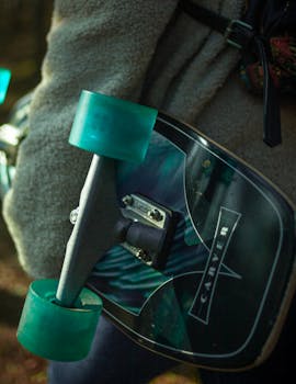Detailed view of a skateboard with teal wheels being held outdoors.