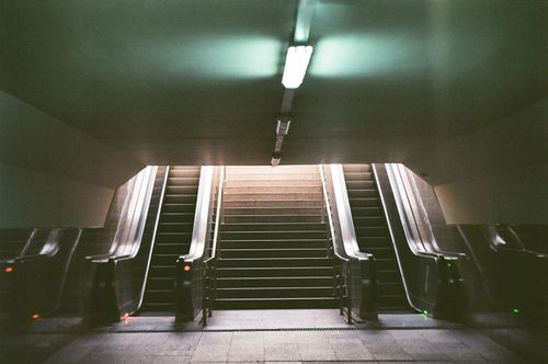 Free A modern urban subway entrance featuring escalators and stairs inside a dimly lit station. Stock Photo