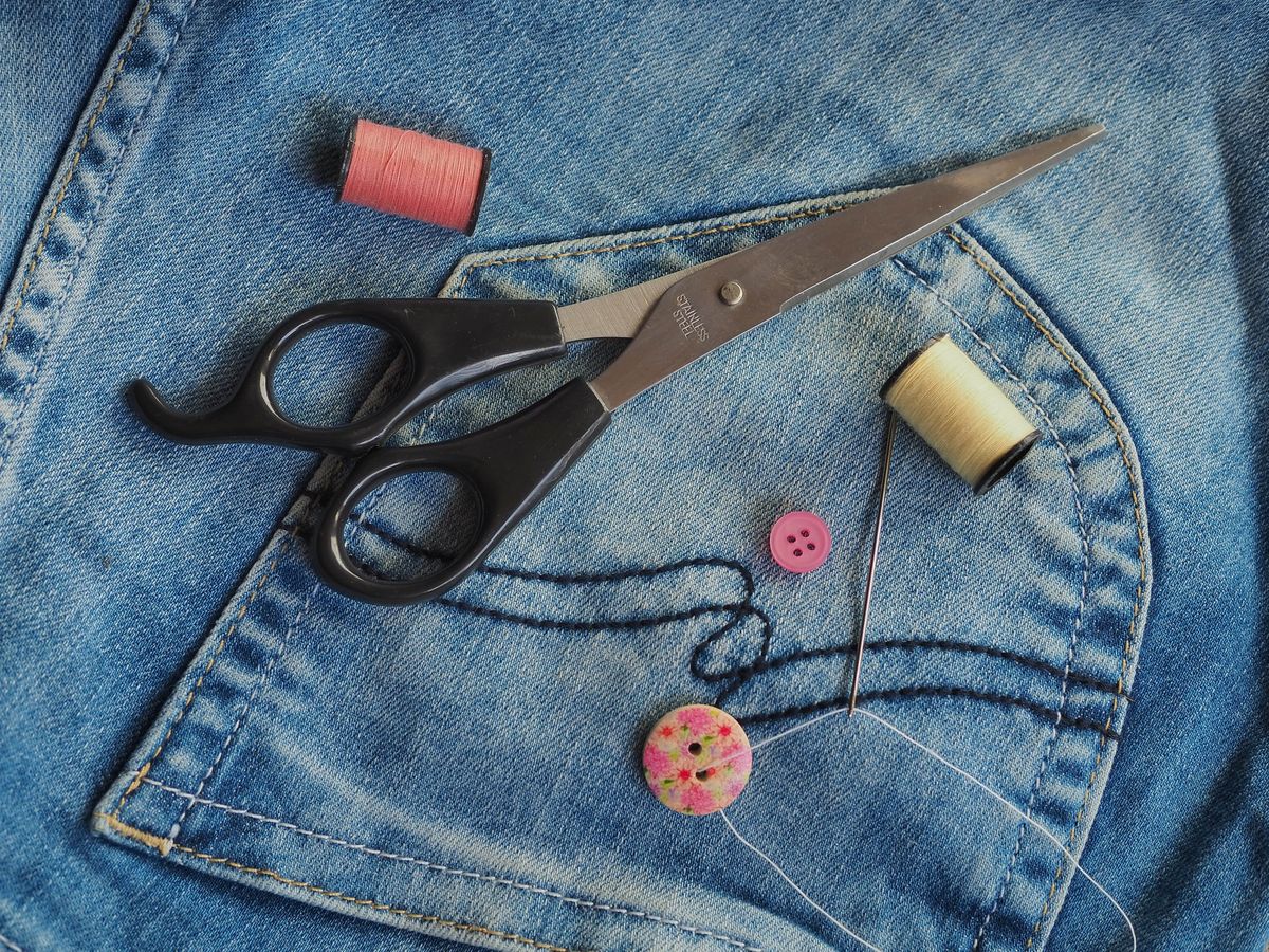 Schere und bunte Nähfäden auf Denimstoff