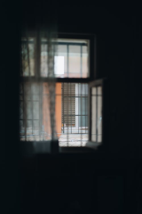Photo of a Silhouetted Interior and View of a Building through an Open Window 