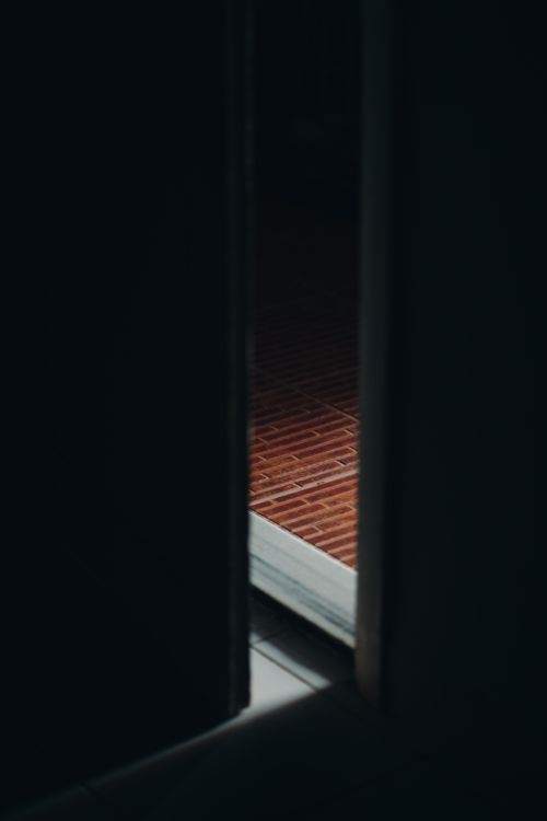 Free A mysterious view through an ajar door revealing a brick floor in a dimly lit room. Stock Photo