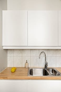 Elegant minimalist kitchen with stainless steel sink, lemon, and white cabinets.