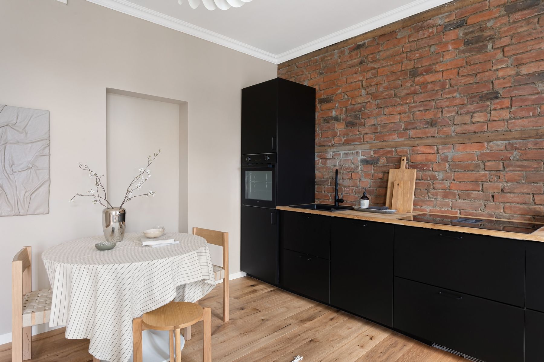 Black cabinet run beneath an exposed brick wall beside a small wood dining table